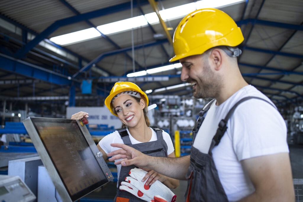 Factory worker explaining trainee how to operate industrial machine using new software on touch screen computer. Software de Indústria e Produção