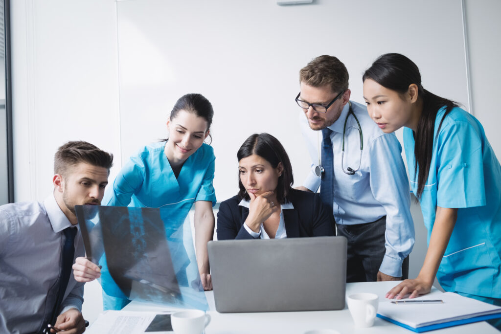 Medical team examining an x-ray report in conference room software de gestão para saúde